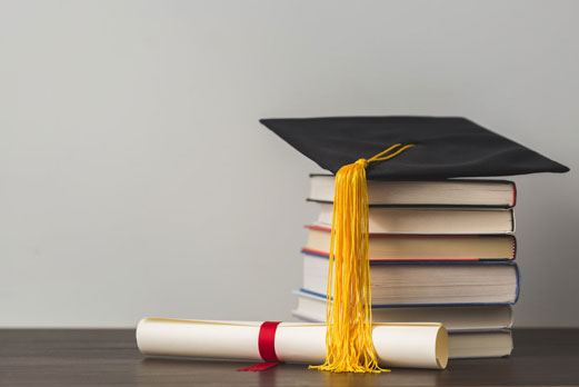 Stack of books that are holding a graduation hat, and a diploma at the bottom of it.